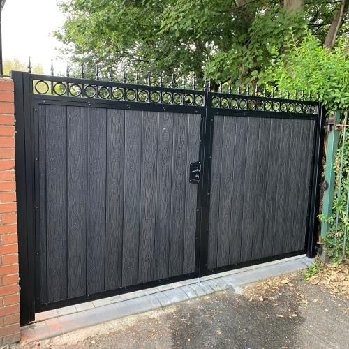 Black steel driveway gates with composite infill panels and decorative finial detail.